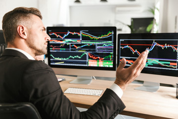 Fototapete - Image of serious businessman working in office and looking on computer with graphics and charts