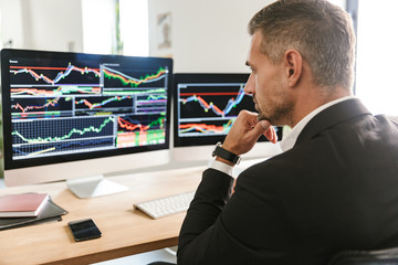 Fototapete - Image of concentrated businessman working in office and looking on computer with graphics and charts at screen
