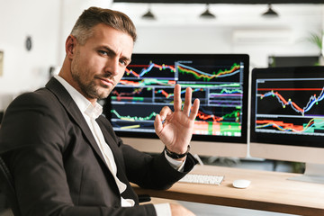 Fototapete - Image of unshaved businessman working in office on computer with graphics and charts at screen