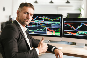 Fototapete - Image of confident businessman working in office on computer with graphics and charts