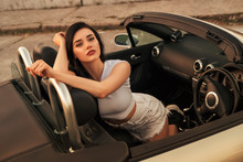 Gorgeous Sexy Woman On A Vacation Car Trip In Summer Day. Luxury Grey Sport Car. Sexy Fit Brunette Woman In Casual Outfit. Sunset