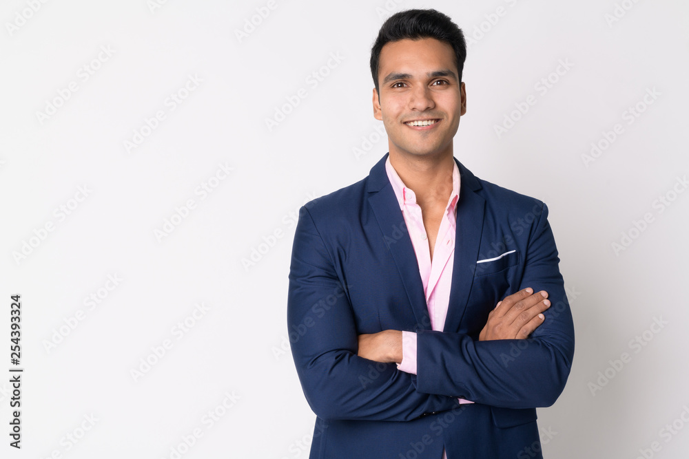 Portrait of young happy Indian businessman in suit smiling with arms ...