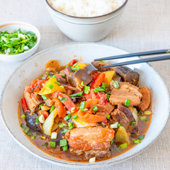 Fried pork with eggplants and sweet peppers in a large bowl and a cup of rice - a traditional Asian dish