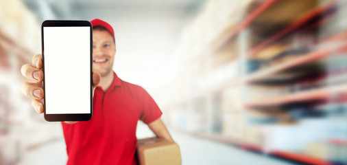 Wall Mural - young smiling delivery service courier showing blank smart phone at warehouse. copy space