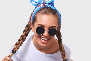 Close up portrait of young pretty woman wearing white t-shirt, blue headband and sunglasses with braids hairstyle, isolated on white background