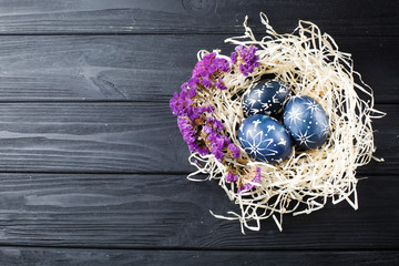 Hand painted dark blue easter eggs in nest and flowers on wooden table