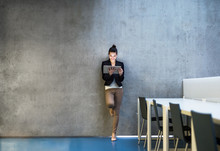 Young Business Woman With Tablet Standing Against Concrete Wall In Office.