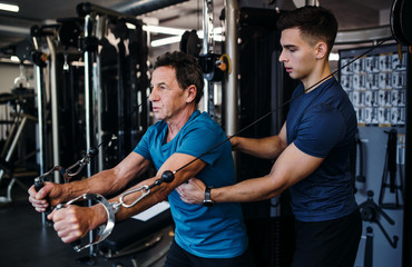 Wall Mural - A senior man with a young trainer doing strength workout exercise in gym.