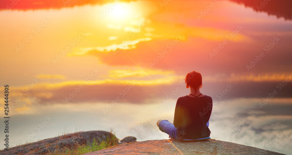 Beautiful woman sits in a pose of a half lotus on high place amazing view of the lake sunset, practice yoga meditation. Kundalini energy. Solitude harmony, mental freedom concept. - obrazy, fototapety, plakaty 
