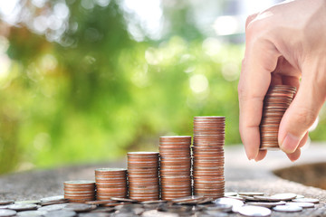 Save money concept with Hand holding coins and coin stack on blur background