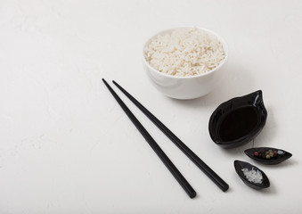 White bowl with boiled organic basmati jasmine rice with black chopsticks and sweet soy sauce on white background. Space for text