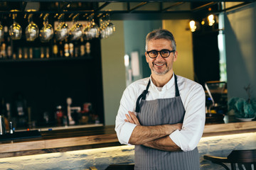 senior barman crosses arms standing in front of counter in cafe bar