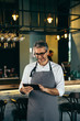 © cherryandbees - middle aged barman using tablet in cafe bar