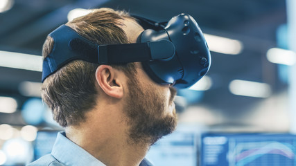 Fototapete - Portrait Shot of the Industrial Engineer Wearing Virtual Reality Headset and Gesturing with Controllers. In the Background Out of Focus Displays and Manufacturing Plant.