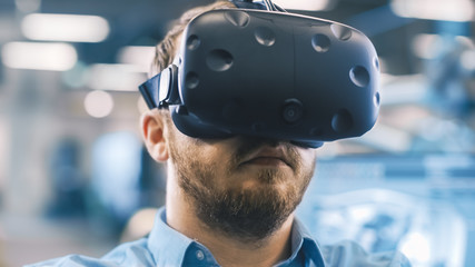 Fototapete - Portrait Shot of the Industrial Engineer Wearing Virtual Reality Headset and Gesturing with Controllers. In the Background Out of Focus Displays and Manufacturing Plant.