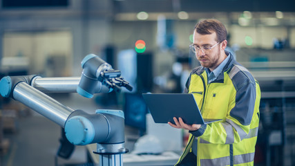 Poster - At the Factory: Automation Engineer Uses Laptop for Programming Robotic Arm. New Era in Automatic Manufacturing Industry.