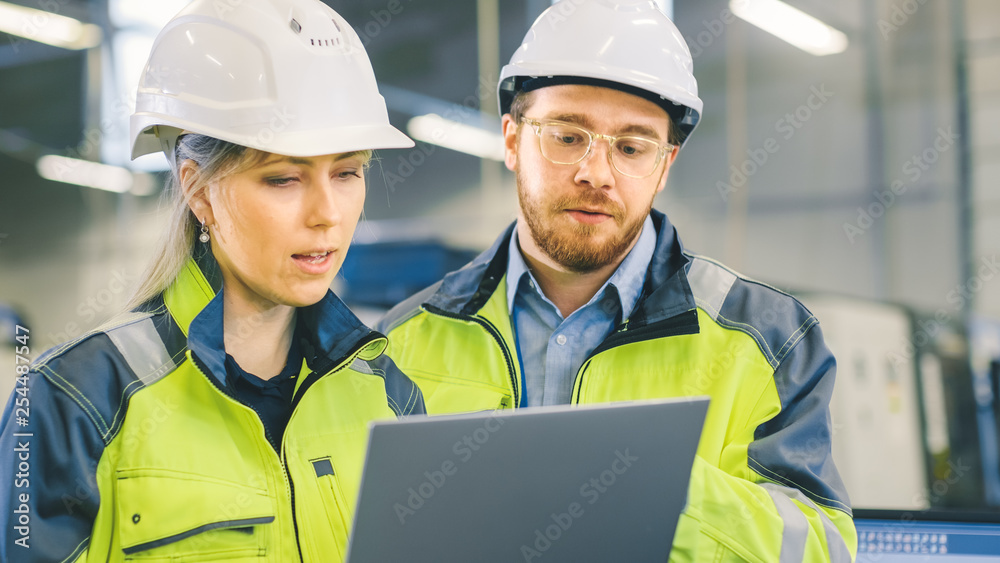 Male and Female Industrial Engineers Work on a Manufacturing Plant, They Discuss Project, Point in the Direction of the Machinery while Using Laptop.  - obrazy, fototapety, plakaty 