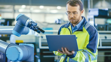 Poster - At the Factory: Automation Engineer Uses Laptop for Programming Robotic Arm. New Era in Automatic Manufacturing Industry.