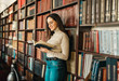© proimagecontent - Student woman standing with opened book and prepare to exams at the library