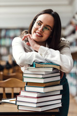 Wall Mural - Portrait of brunette teen girl folding hands on the books in library