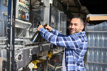 Wall Mural - young man wine maker working filling wine bottle with automatic bottling machine