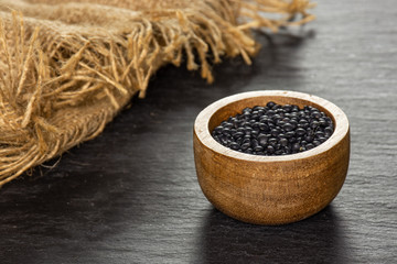 Lot of whole black lentils beluga variety with wooden bowl on grey stone