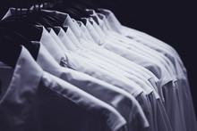 Row of white shirts hang on hangers in the darkness of a wardrobe, toned in blue.