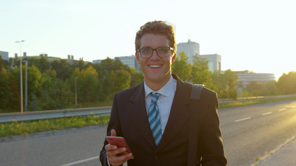 Wall Mural - PORTRAIT: Carefree businessman smiling at camera while walking along sunlit road