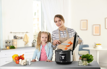 Canvas Print - Mother and daughter preparing food with modern multi cooker in kitchen