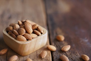 Wall Mural - Almond nut in wood bowl on wooden table with green leaf background