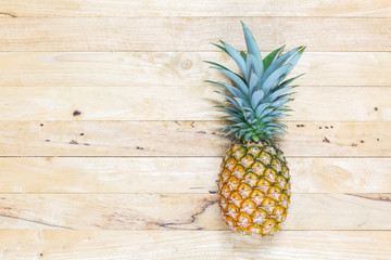 Wall Mural - Single whole pineapple with green leaves on the wooden texture background.