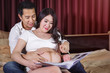 happy pregnant woman and her husband looking ultrasound scan photo album on bed