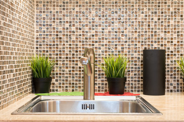 Metal sink with metal faucet on the artifical stone countertop and pots with green grass