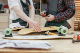 Fototapeta  - Two unknown male carpenters make a skateboard on an exclusive order. Concept hobby for youth and handmade