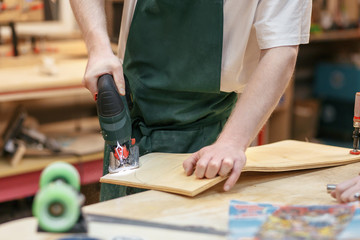 Unidentified male carpenter jigsaw out the base for a skateboard. Concept of a professional workshop for wood processing