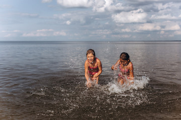 Cheerful two girls playing on the ocean or sea beach having fun together, playing with water. Childhood, summer vacation, happines concept