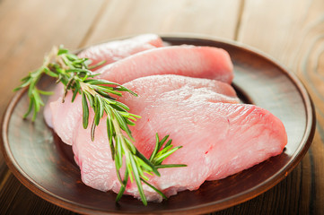 Chicken fillet with rosemary on a wooden plate on a textural table. Raw turkey meat and peppercorns close-up and copy space.