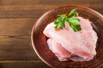 Chicken fillet with a sprig of parsley on a wooden plate on a textural table. Raw turkey meat close up and copy space.