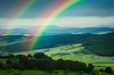 Fototapeta Tęcza - rainbow over beautiful green summer landscape after rain, fresh green meadows and hills in serene landscape