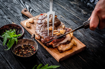 Hands cutting grilled meat with garlic on a wooden board