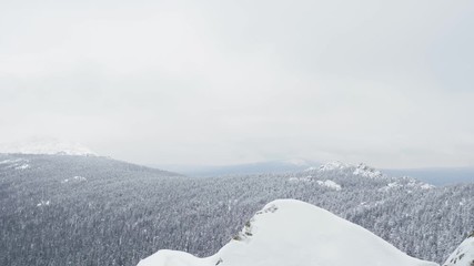 Wall Mural - A young man, a tourist with a backpack, stands on the edge of the mountain next to the cliff, arms outstretched to the side, and admires the view of the top of the mountain. Winter season.