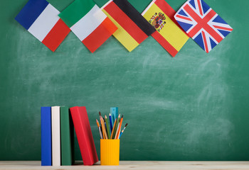 Fototapete - backpack, flags of Spain, France, Great Britain and other countries, books and school supplies of the blackboard