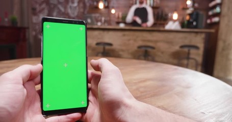 Handheld shot of man with a green screen smartphone in a vintage pub, coffee shop or restaurant. The man is calling the waiter