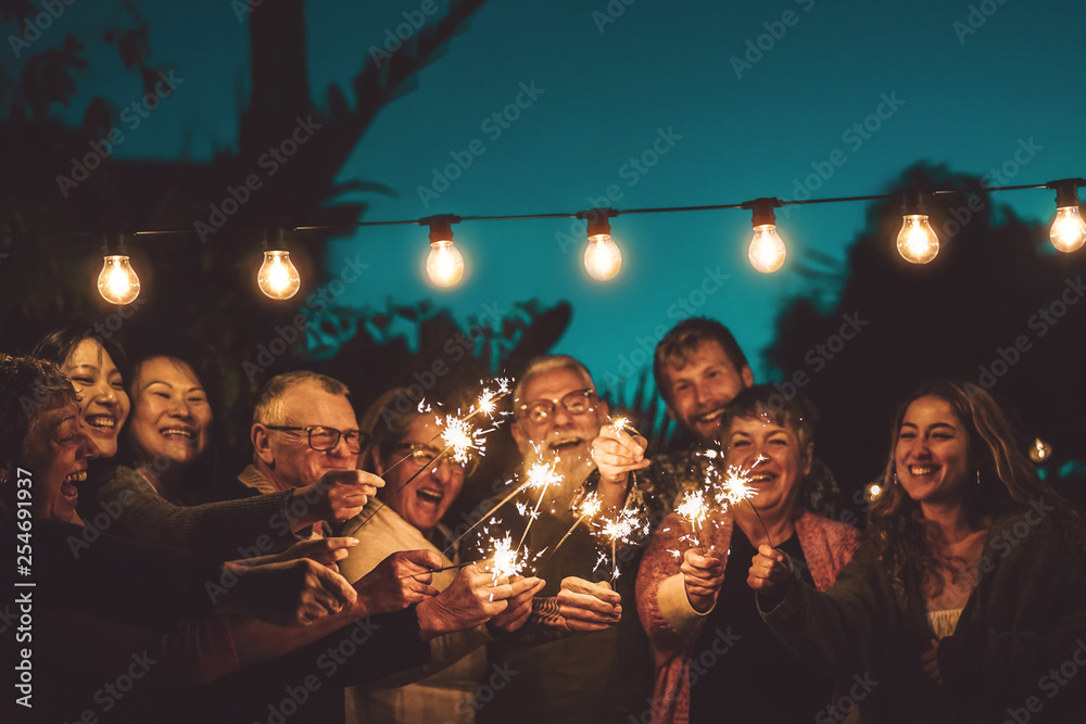Happy family celebrating with sparkler at night party outdoor - Group of people with different ages and ethnicity having fun together outside - Friendship, eve and celebration concept - obrazy, fototapety, plakaty 
