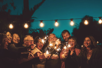 Happy family celebrating with sparkler at night party outdoor - Group of people with different ages and ethnicity having fun together outside - Friendship, eve and celebration concept