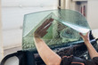 © Aleksandr Kondratov - The wizard for installing additional equipment sticks a tint film on the side front glass of the car and flattens it by hand to fit the glass with a greenish tint in the auto service.