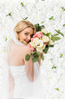 © LIGHTFIELD STUDIOS - beautiful young bride holding wedding bouquet near face on white floral background