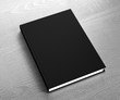 Book template with hard black cover. Gray wooden background. 3D rendering.