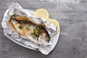 Wall Mural - baked fish with lemon in aluminium foil on ceramic background