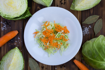 Wall Mural - Salad with cabbage and carrot in the white plate on the brown wooden background.Healthy food ingredients.Top view.Copy space.